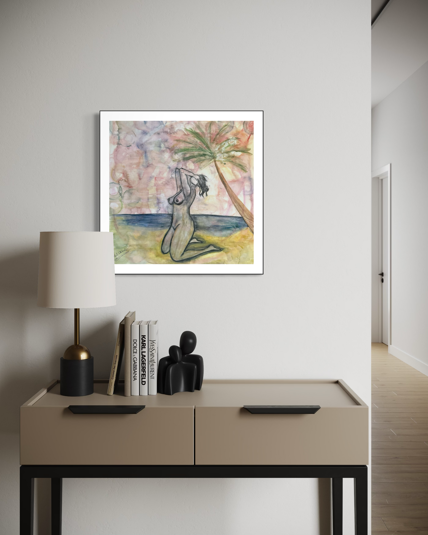 Framed artwork of a nude figure by a beach with a lamp and books on a table below.