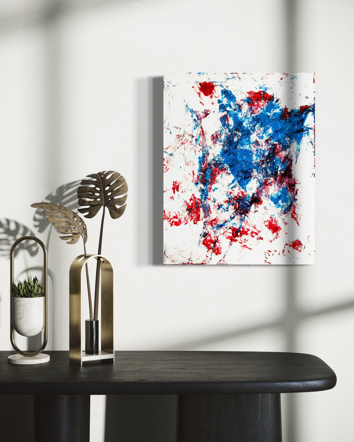 Abstract painting with red and blue splashes on a white wall above a black table.